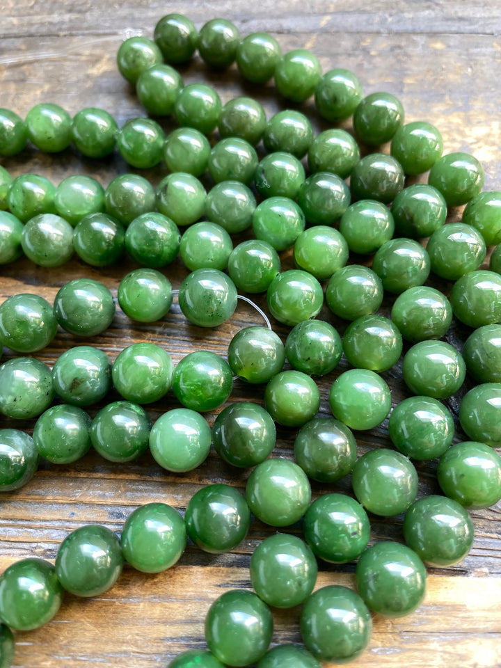 Close up of unstrung green 10mm beads on a wooden surface, glossy round spheres.