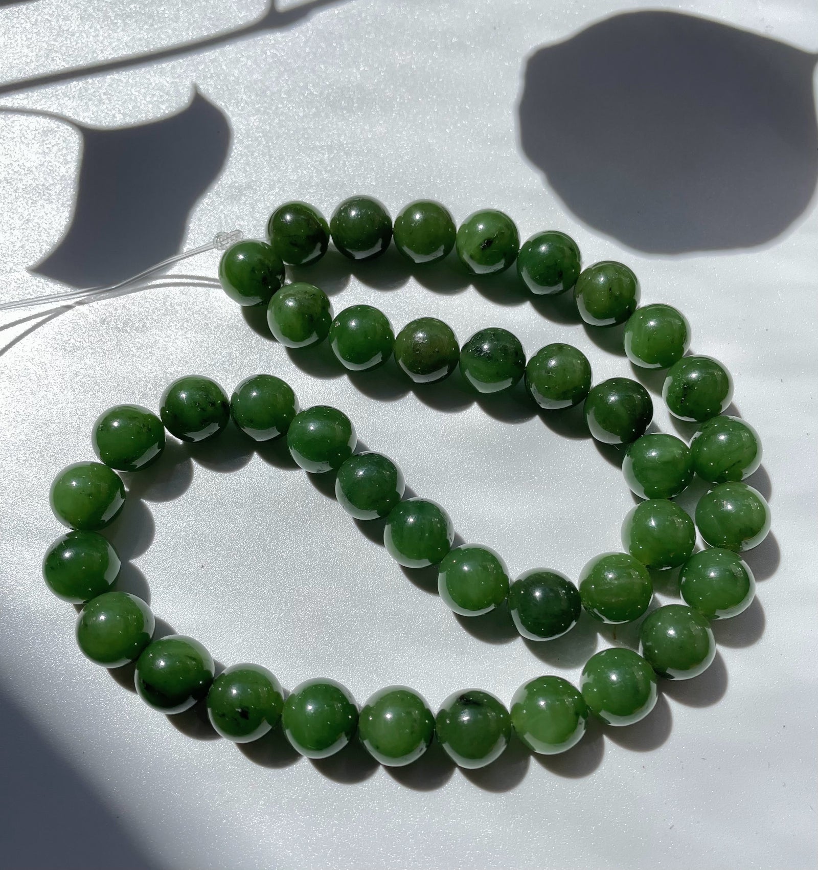 Unstrung 10mm green jade beads on a thin string laid in a coil