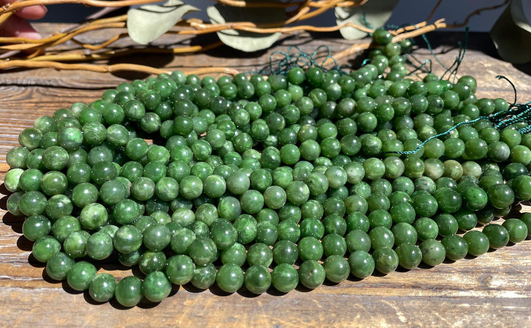 Multiple 8mm green beads on wood with exposed teal string ends ready for stringing.
