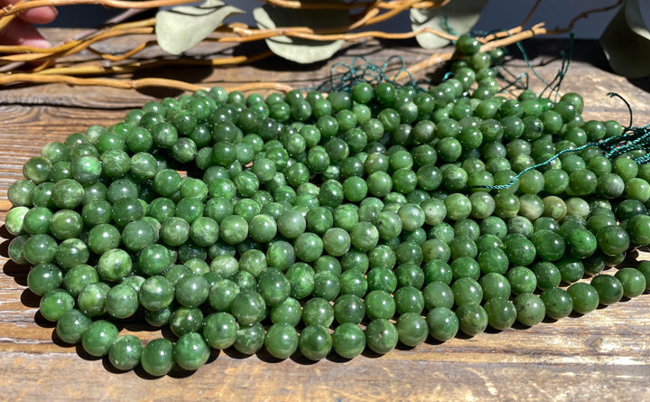 Multiple 8mm green beads on wood with exposed teal string ends ready for stringing.