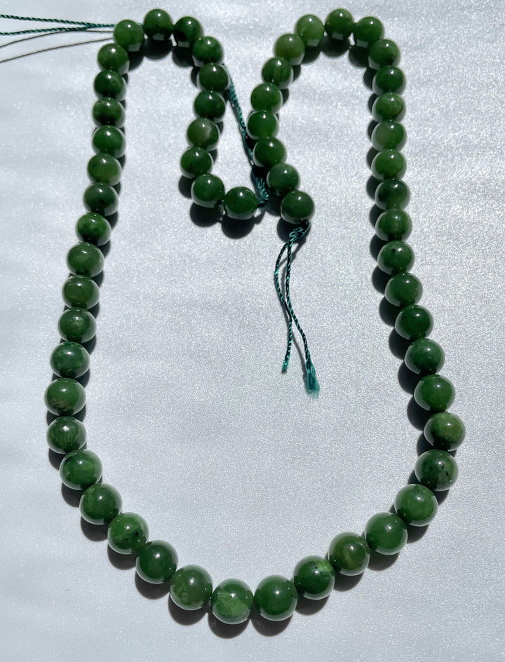 Unstrung 8mm green bead strand with teal thread ends on a light background.