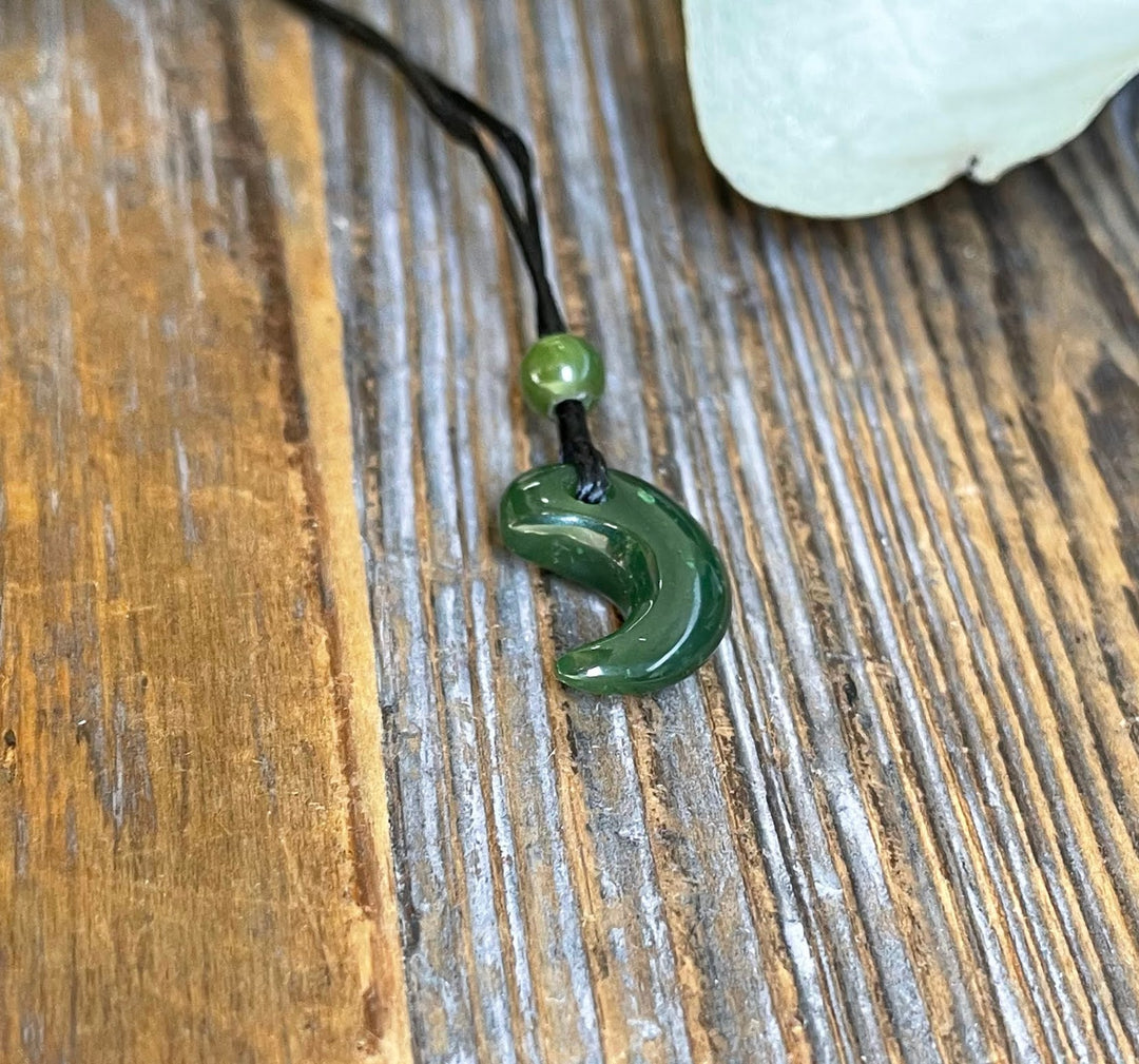 Jade magatama pendant 12x16mm on a black cord with a green bead above, resting on a rustic wood surface