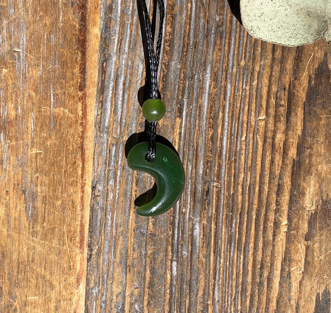 Close-up of jade magatama pendant on a brown cord with a bead, shown against weathered wood