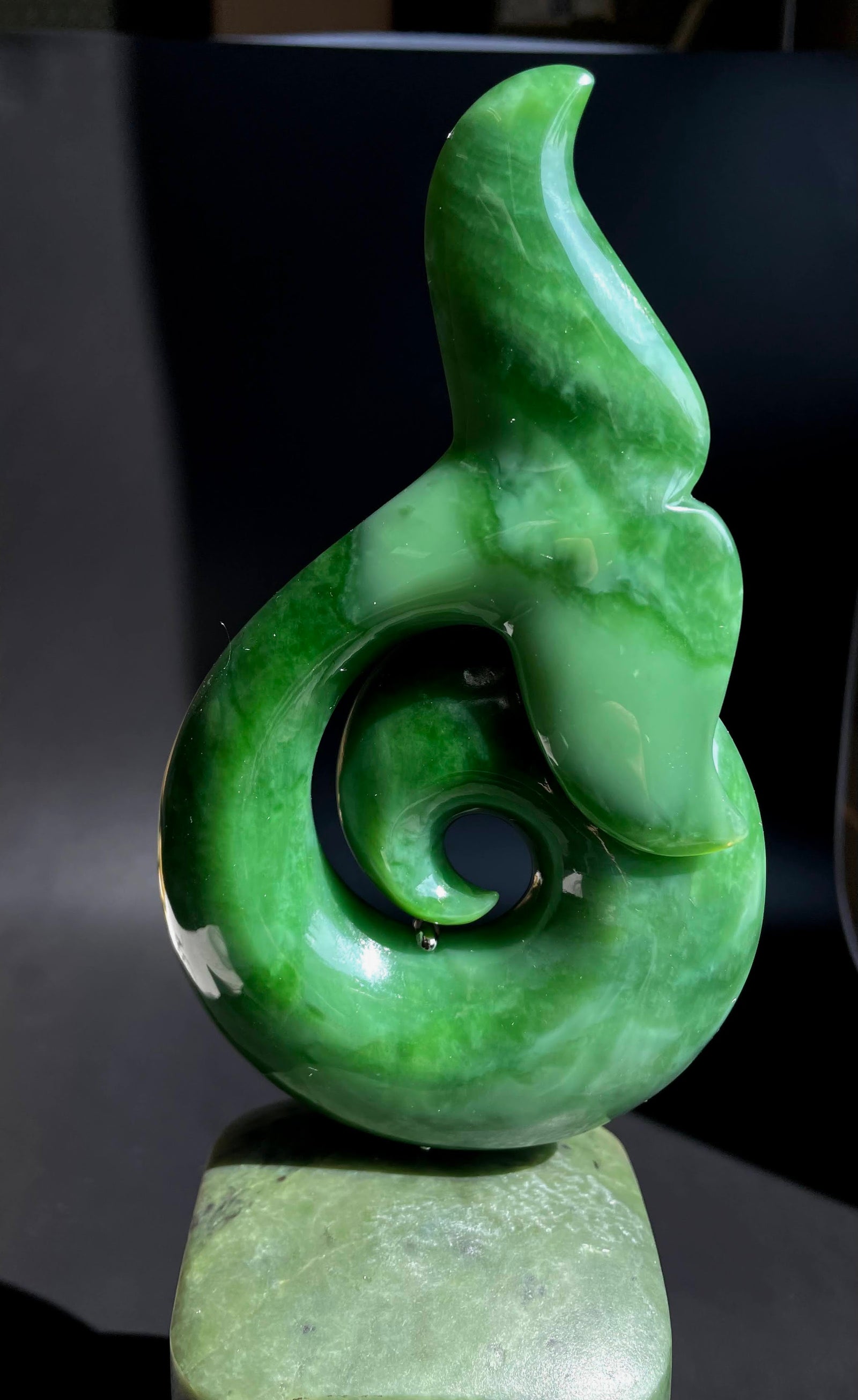 Green jade whale tail sculpture perched on a smooth rounded jade base.