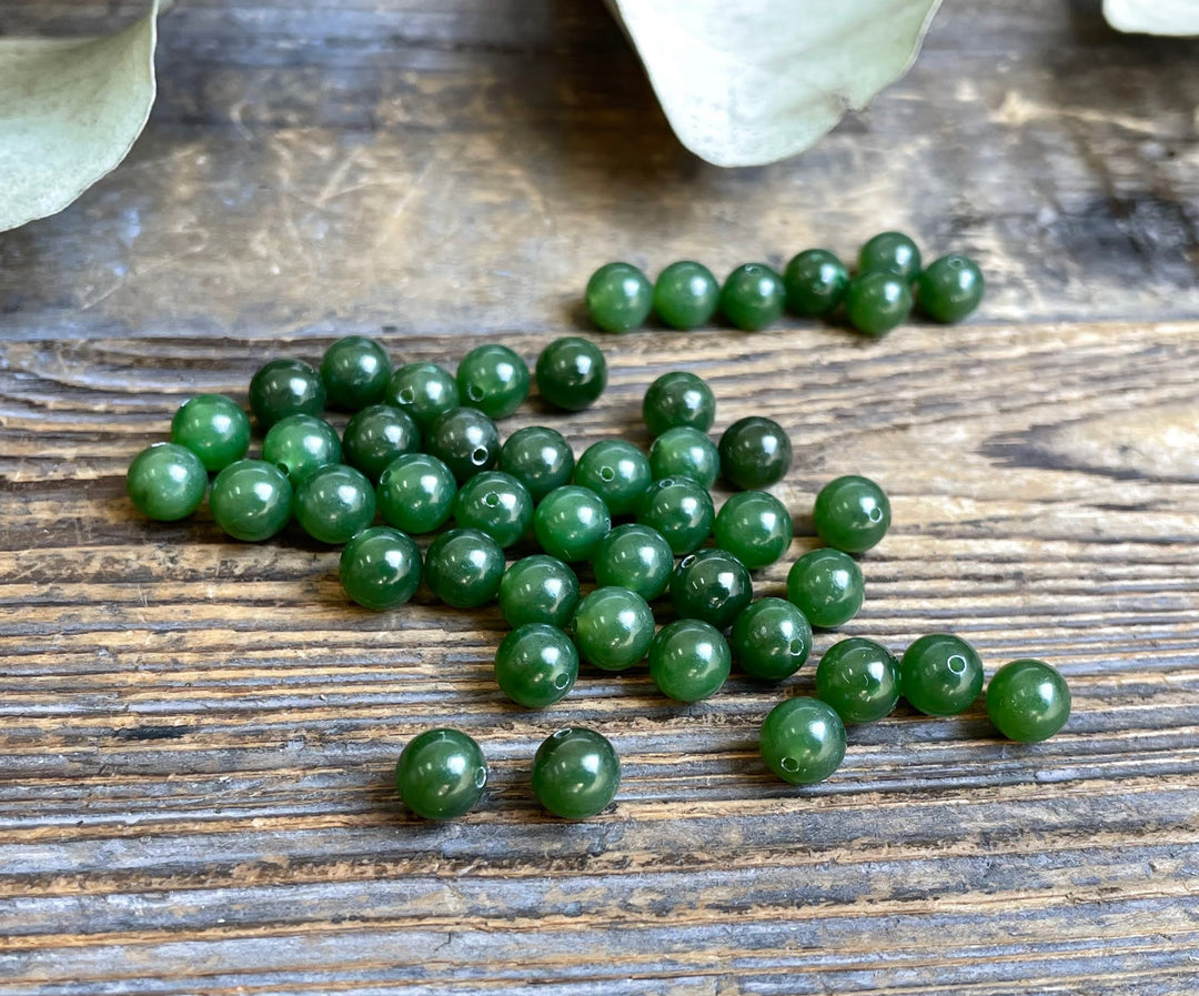 Green Canadian jade half drilled beads 6mm scattered on a rustic wooden surface