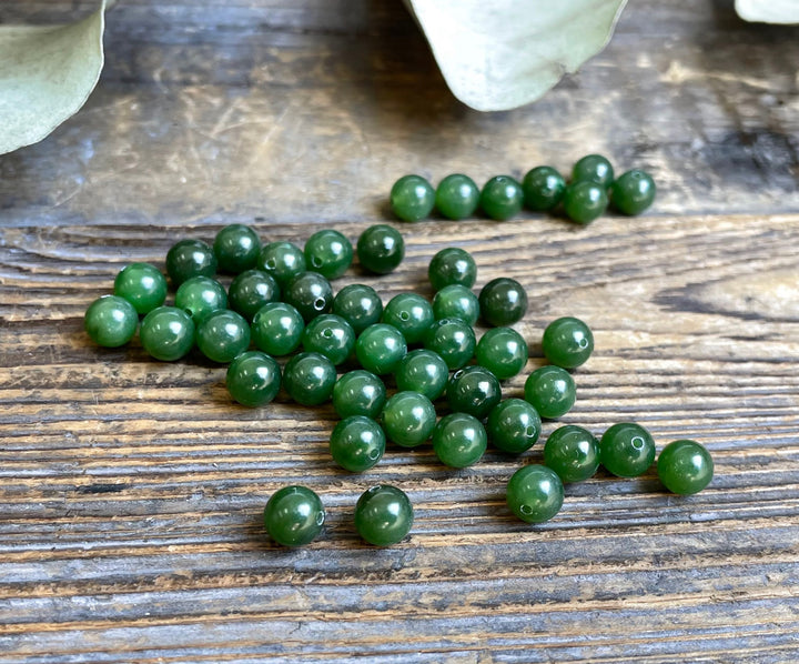Green Canadian jade half drilled beads 6mm scattered on a rustic wooden surface