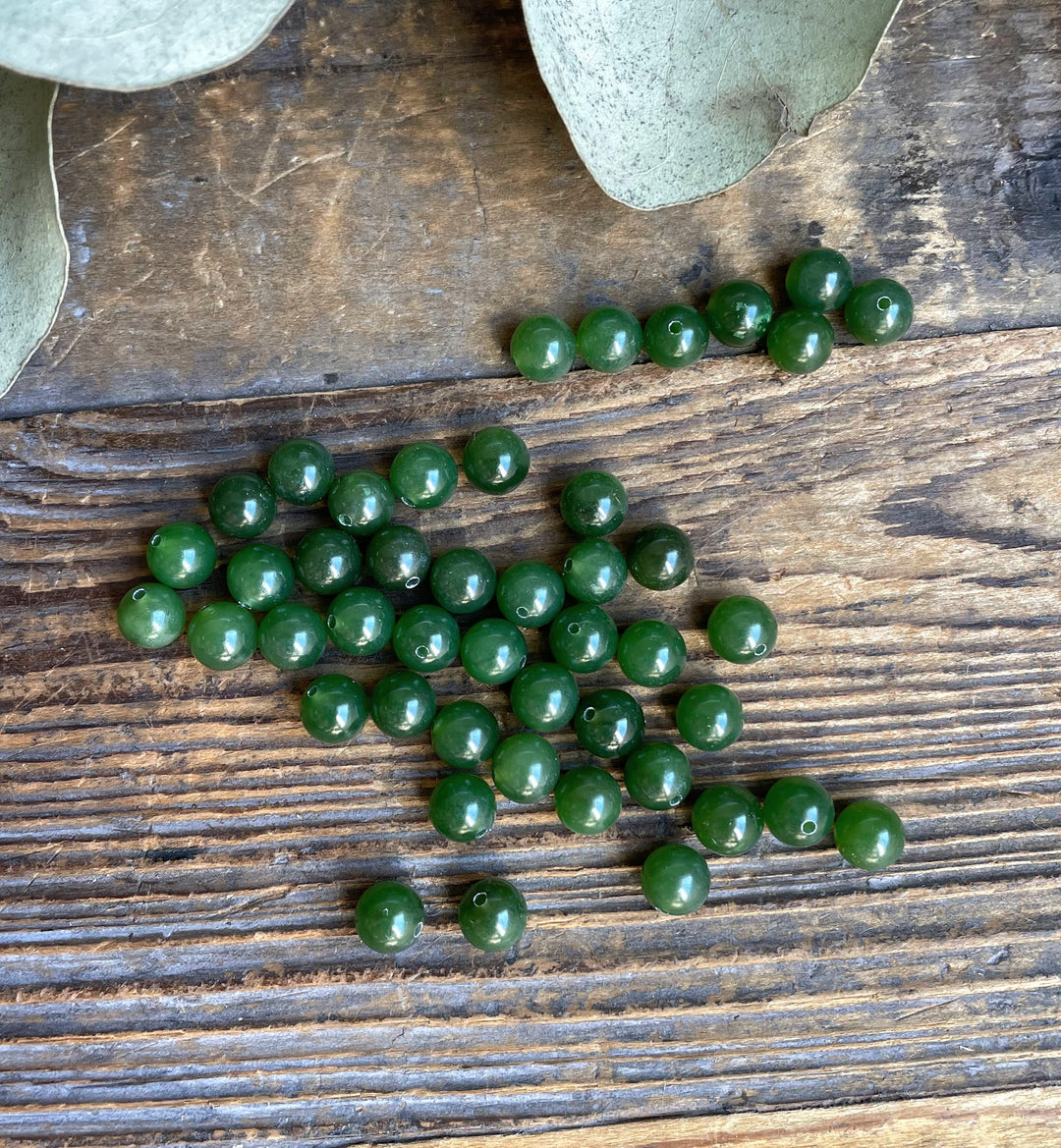 Handful of green Canadian Jade 6mm half drilled beads with eucalyptus leaves in the background