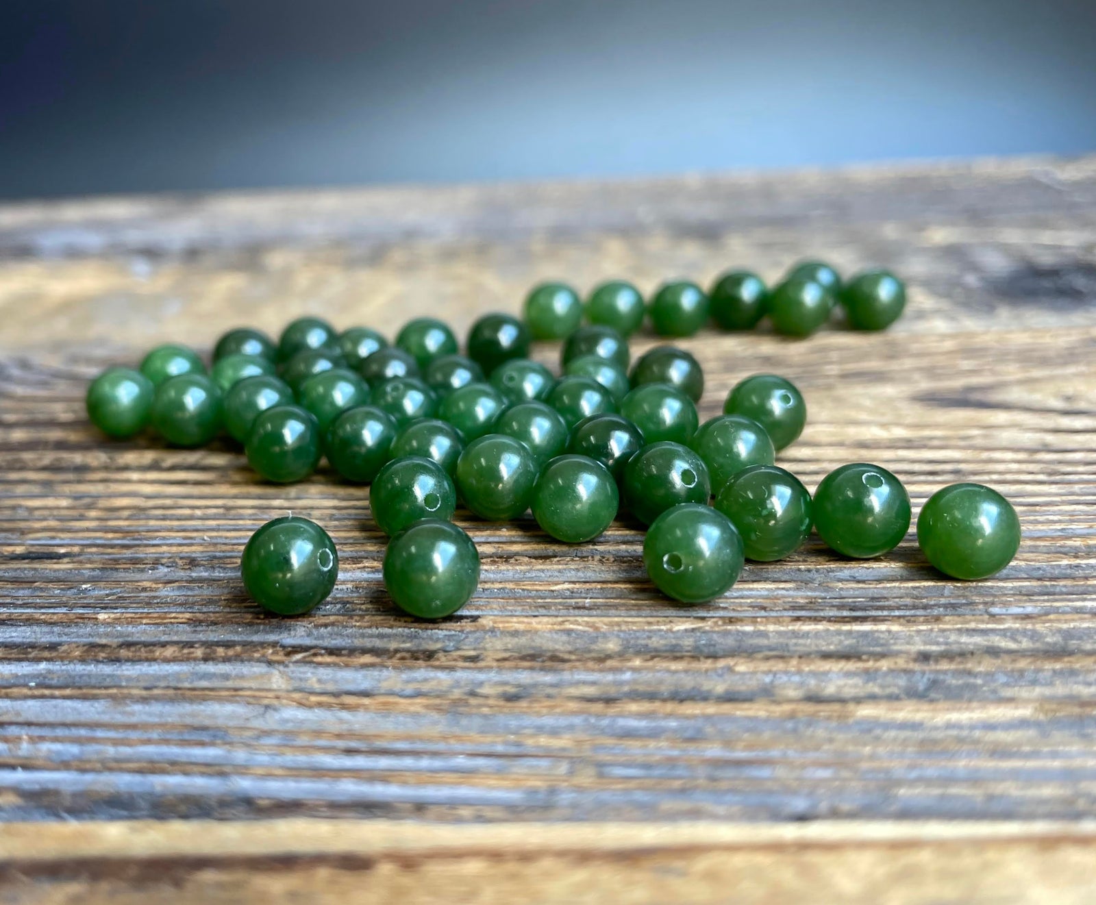 Green Canadian Jade 6mm half drilled beads on a rustic wooden surface