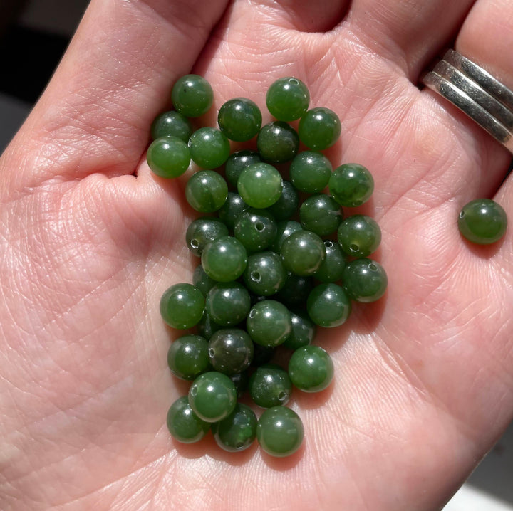 Close up of green Canadian Jade 6mm half drilled beads held in a hand with a silver ring nearby