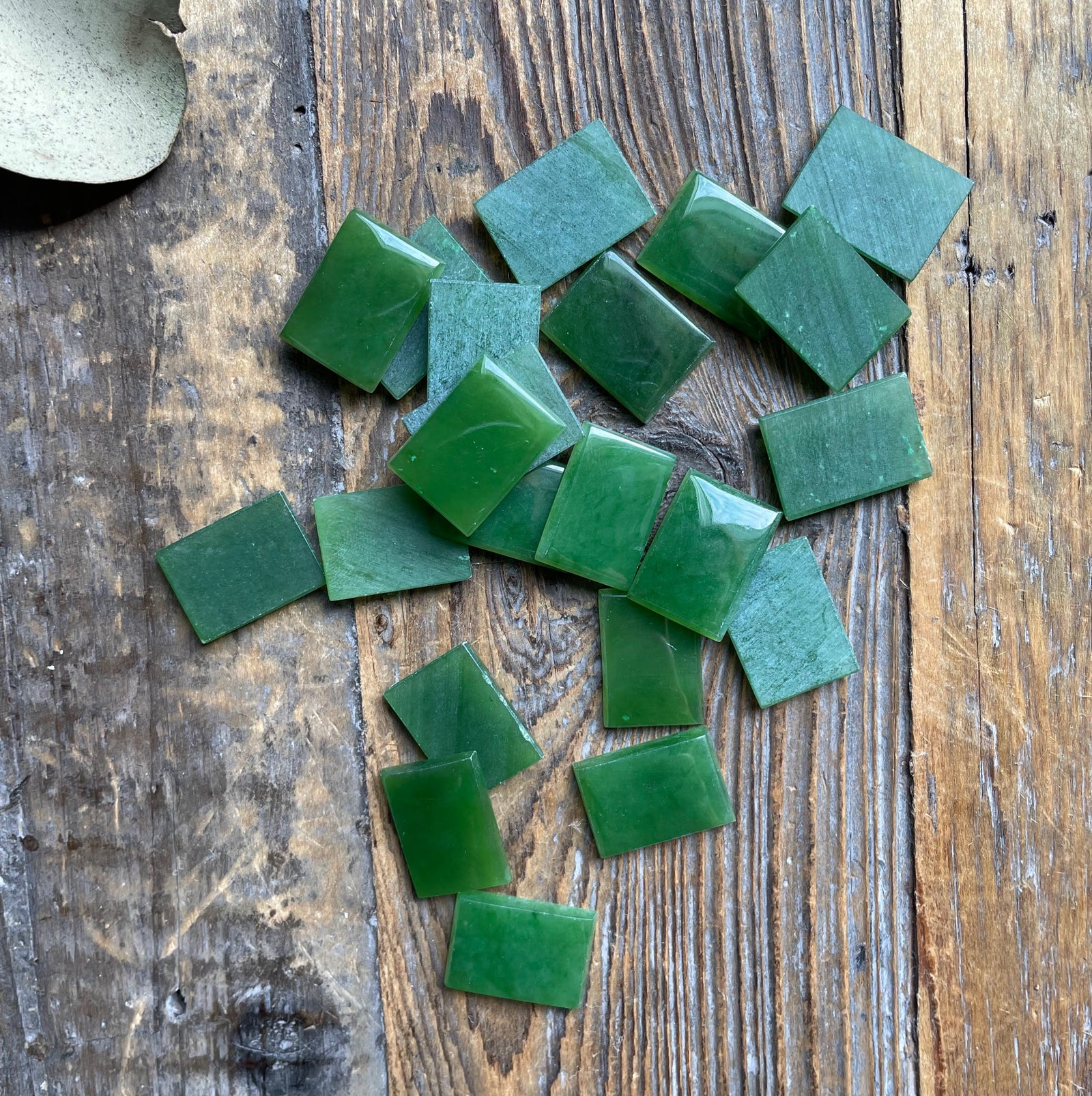 A grade emerald green rectangle cabochons 17.5x12.5mm scattered on a weathered wooden surface