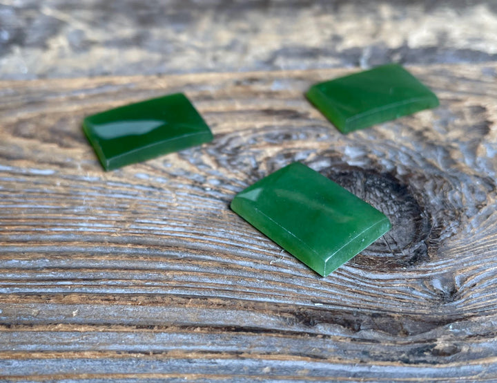 Green rectangle cabochon 17.5 by 12.5 mm resting on a weathered wooden surface