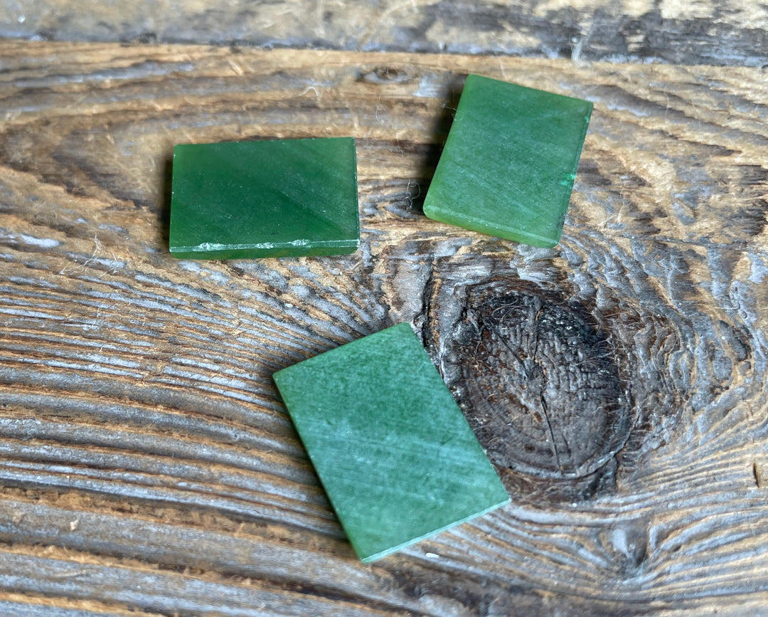 Three green rectangle cabochons arranged on a rustic wooden surface