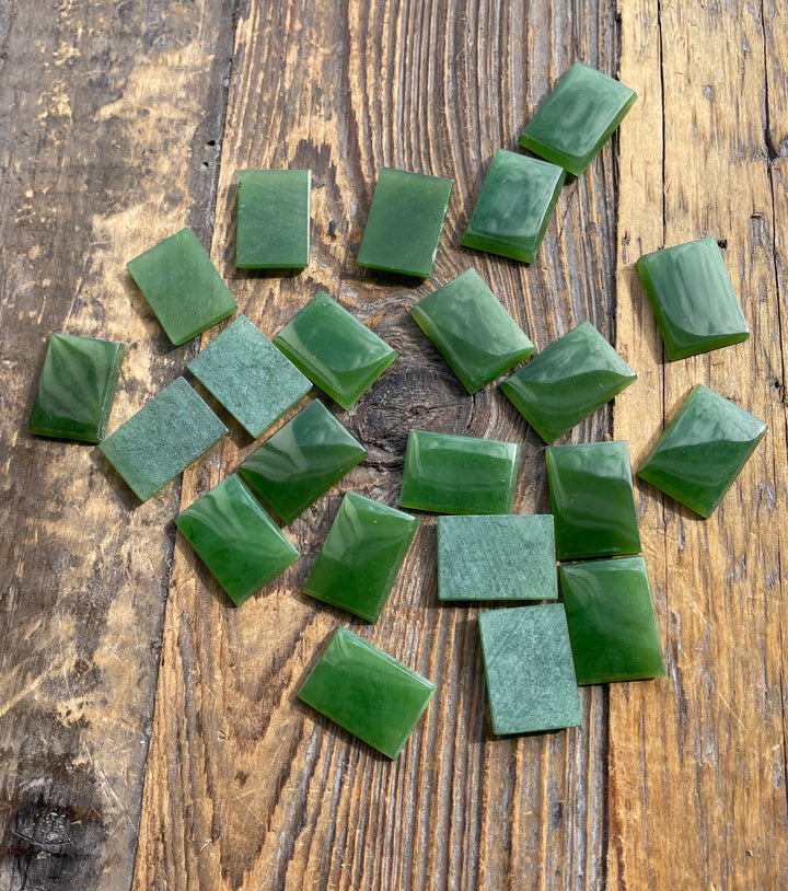 Several green rectangle cabochons scattered over a weathered wooden surface