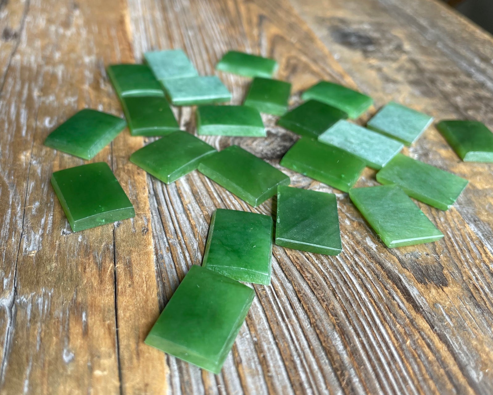 A Grade Rectangle Cabochon 17.5x12.5mm emerald green cabochons scattered on a rustic wooden surface