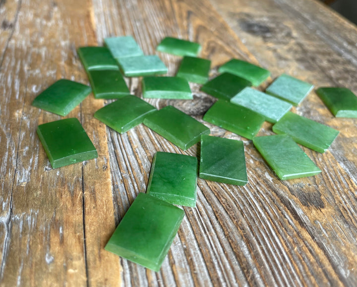 A Grade Rectangle Cabochon 17.5x12.5mm emerald green cabochons scattered on a rustic wooden surface