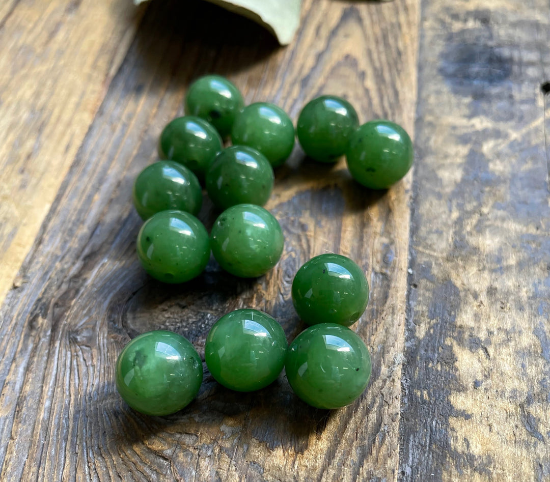 Glossy green 12mm Canadian jade beads scattered on a rustic wooden surface