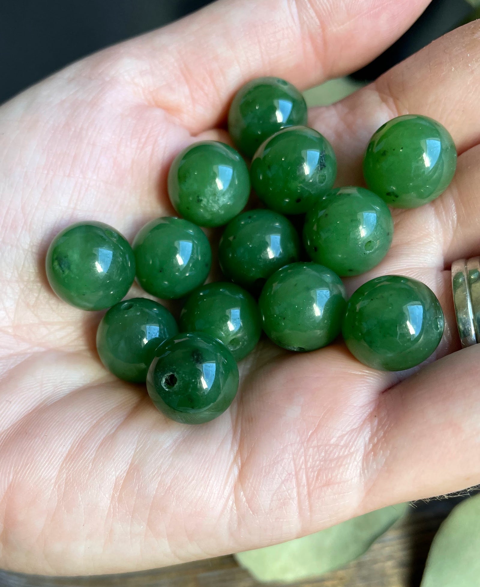 Close up of a green jade bead with a drill hole held in a hand