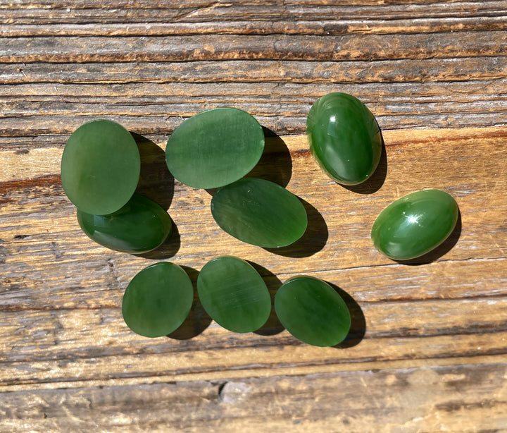 AA Grade Siberian Jade oval cabochons spread on weathered wood board in sunlit light