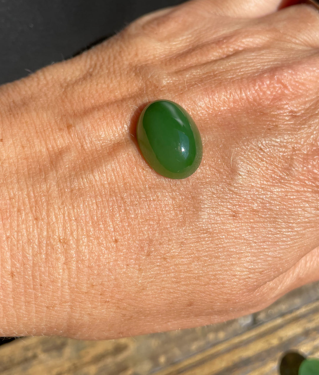 Oval Siberian jade cabochon in bright green resting on a hand.