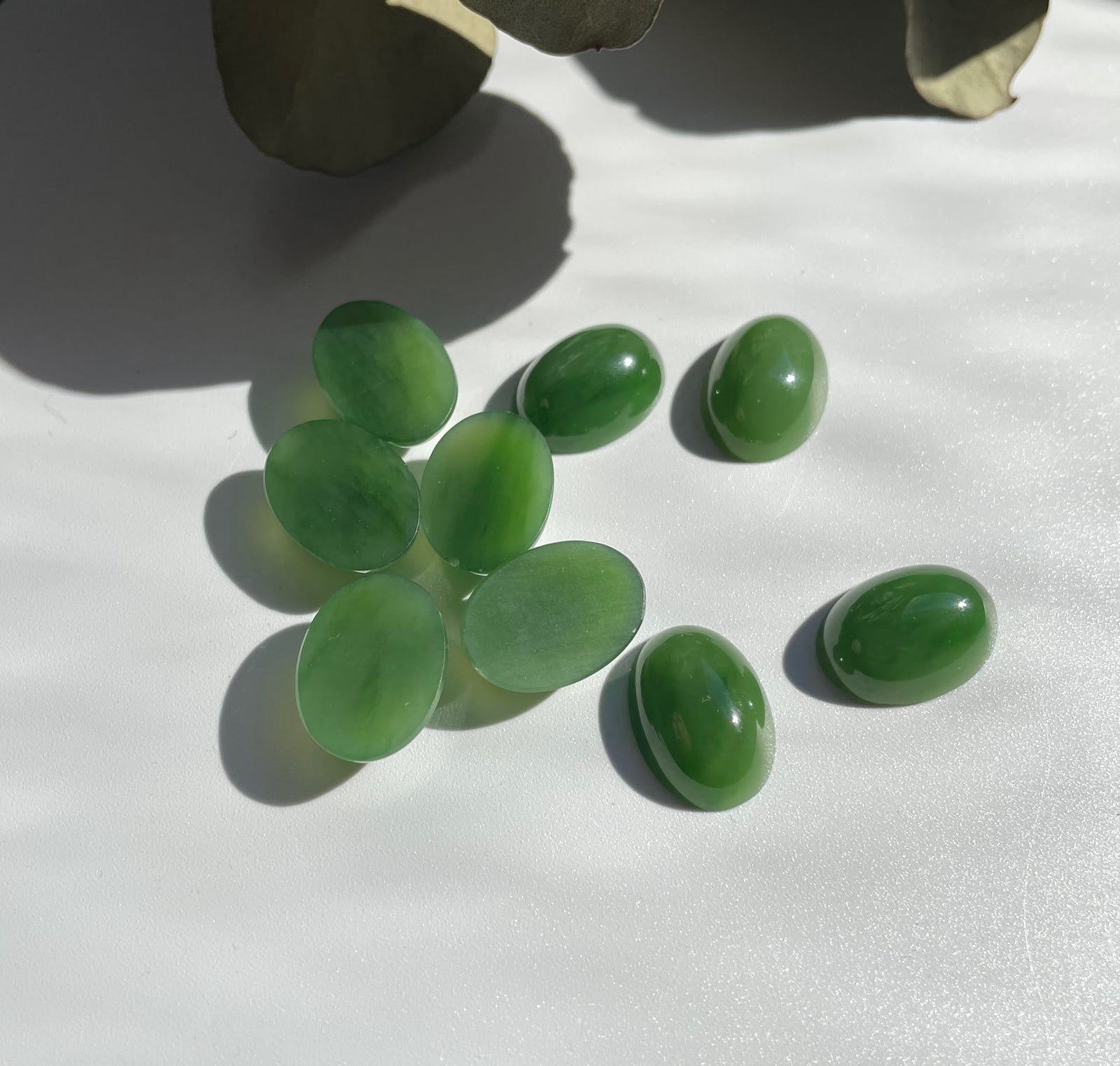 Group of green Siberian jade oval cabochons 18x13 mm on a white surface