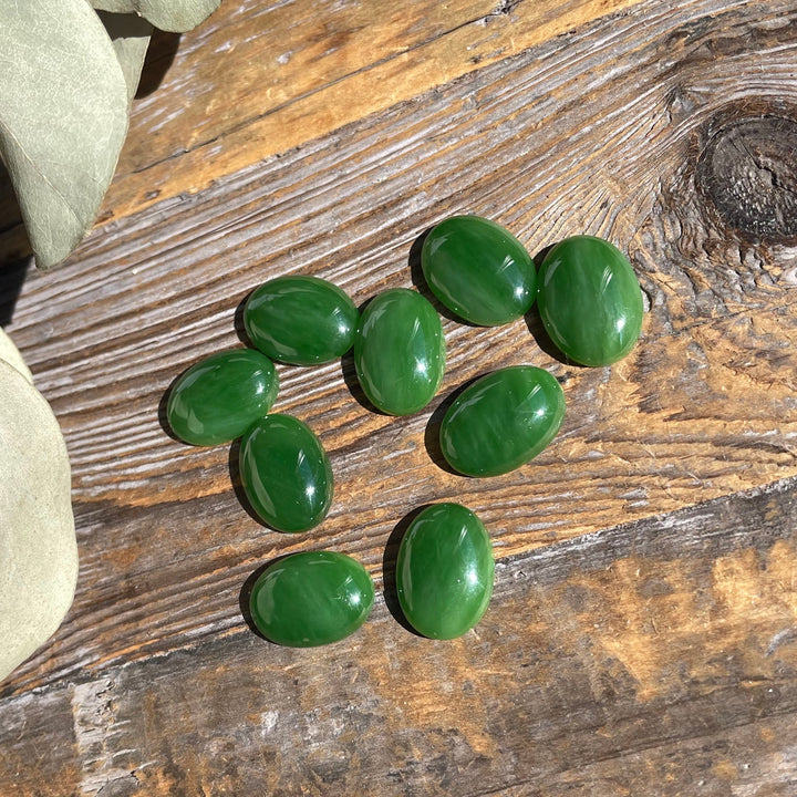 AA Grade Siberian Jade oval cabochons 18x13mm scattered on a wooden surface