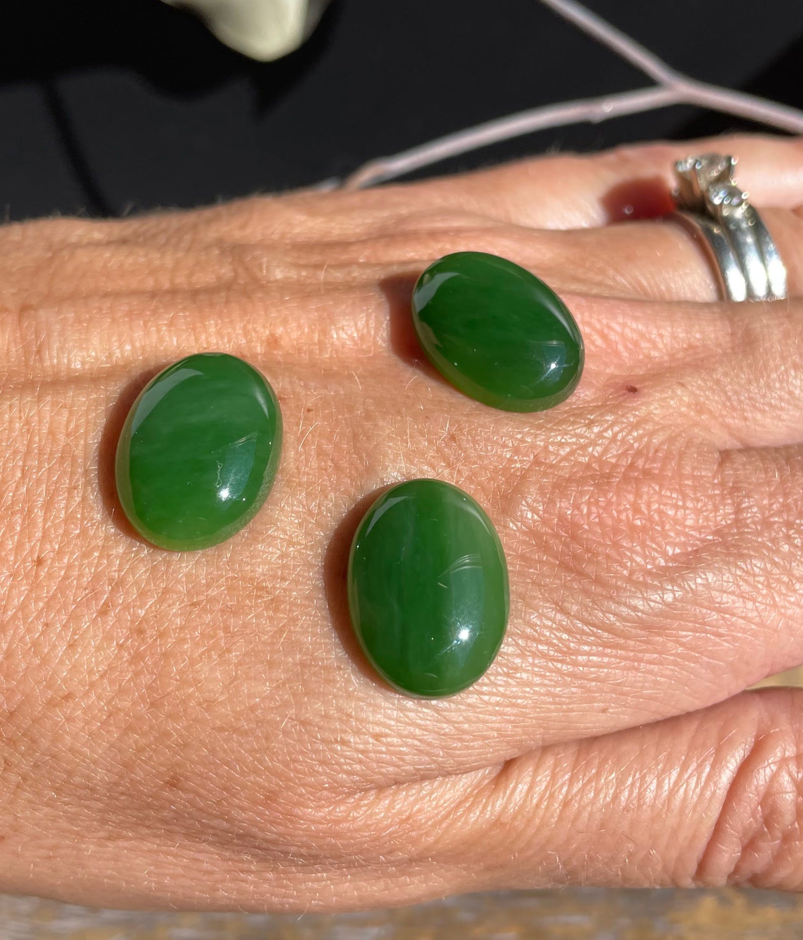 Three AA Grade Siberian Jade oval cabochons 18x13mm on a person's hand