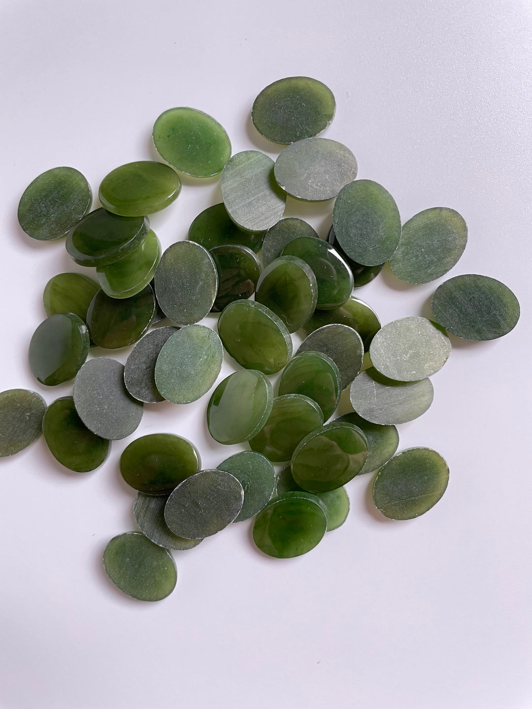 Green jade cabochons with flat backs scattered on a white surface