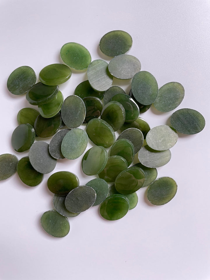 Green jade cabochons with flat backs scattered on a white surface
