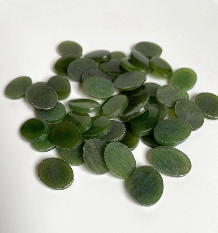 Assorted green jade flat top oval cabochons scattered on a white surface