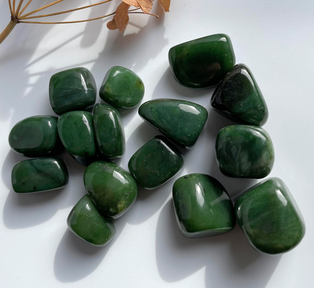 Assortment of green jade nuggets spread on a white surface with a dried plant stem in the background