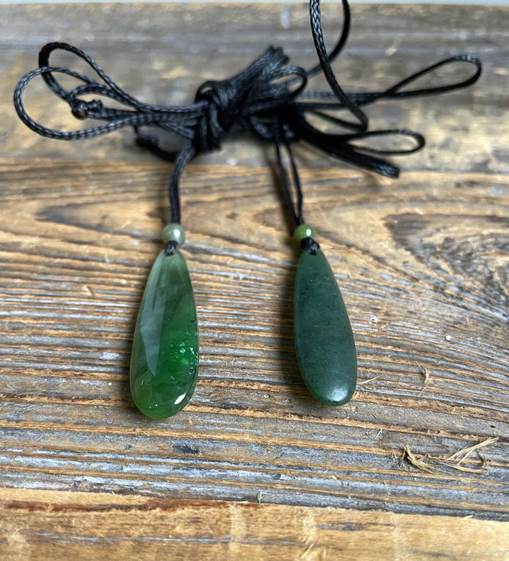 Two green jade drop pendants on black cords with small beads.