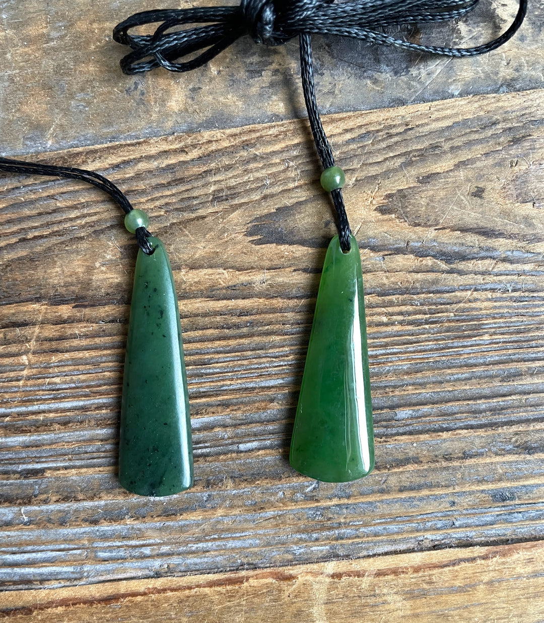 Two green jade drop pendants on black cords with small green beads above