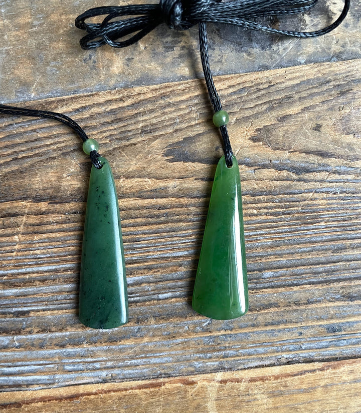Two green jade drop pendants on black cords with small green beads above