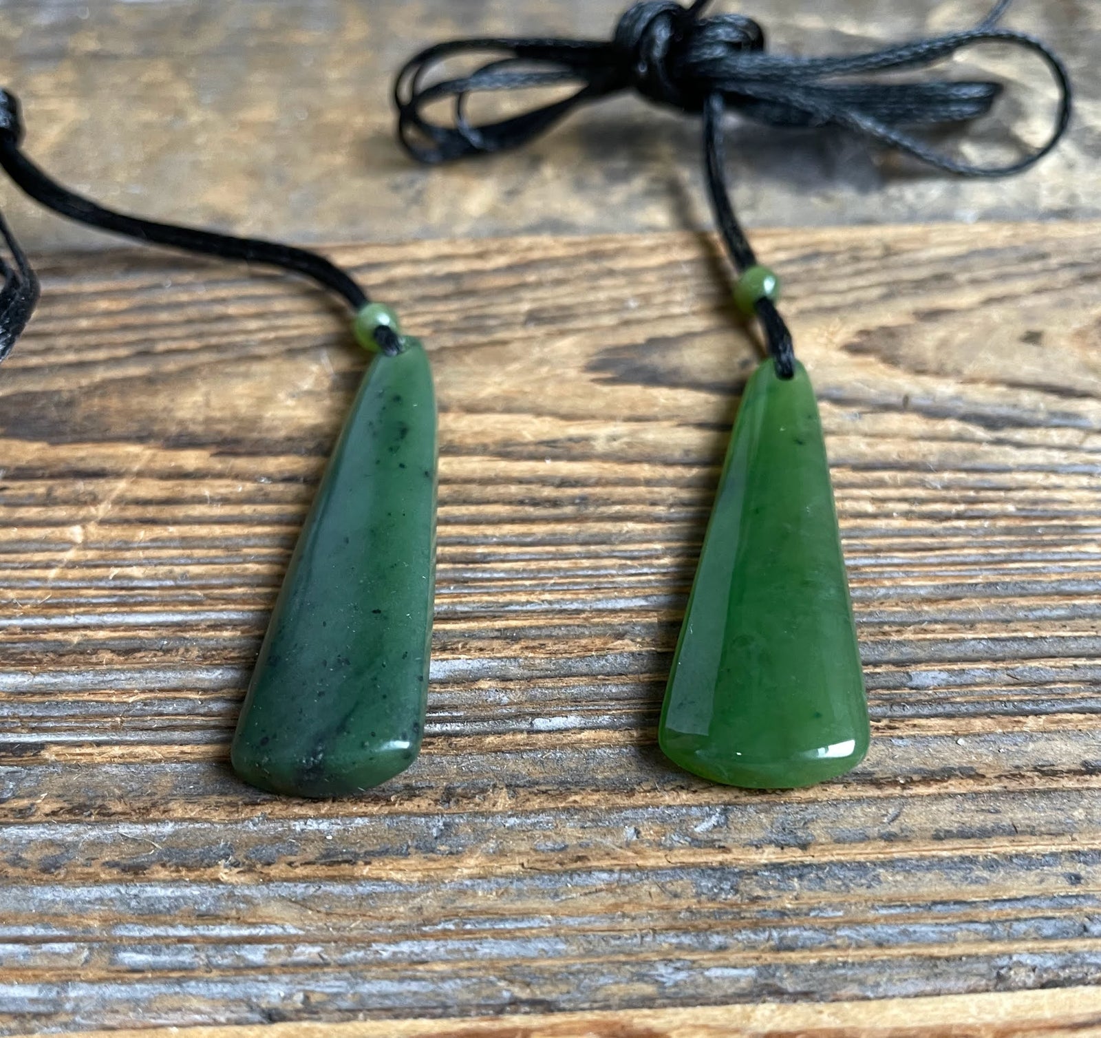 Pair of green jade drop pendants on black cords laid on a wooden surface