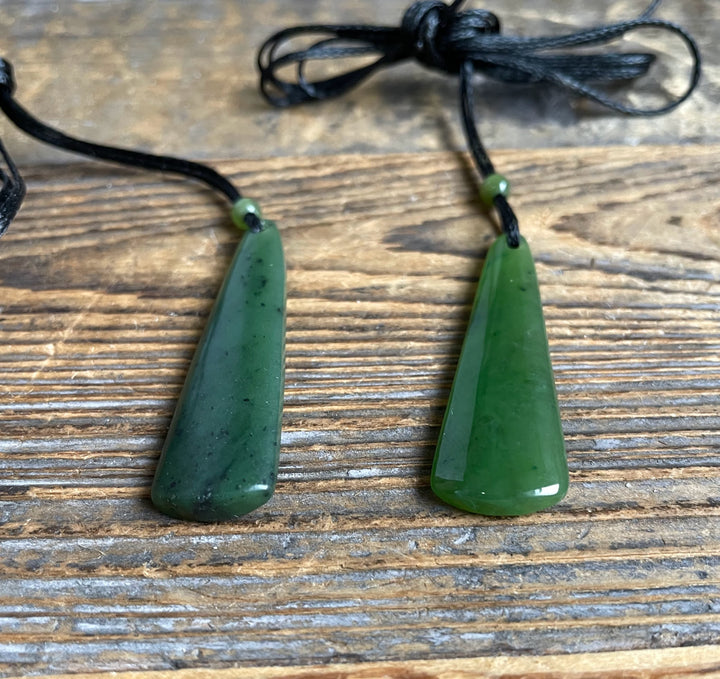 Pair of green jade drop pendants on black cords laid on a wooden surface