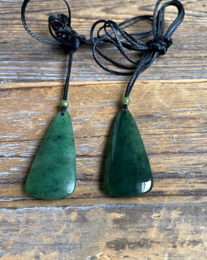 Pair of green jade drop pendants on black cords with small green beads against a wood background