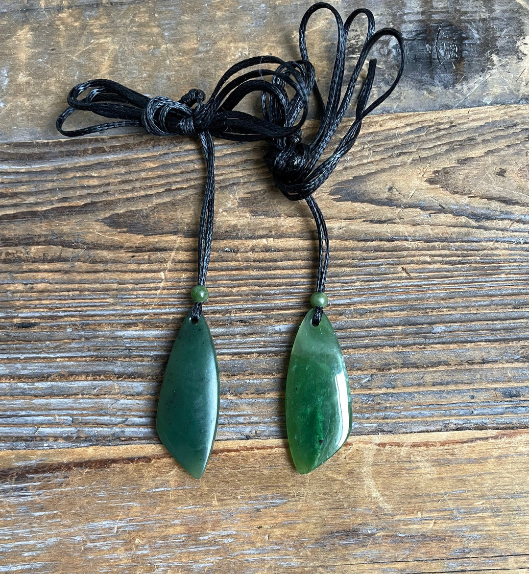 Two green jade teardrop pendants on tangled black cords with small green beads at the top of each