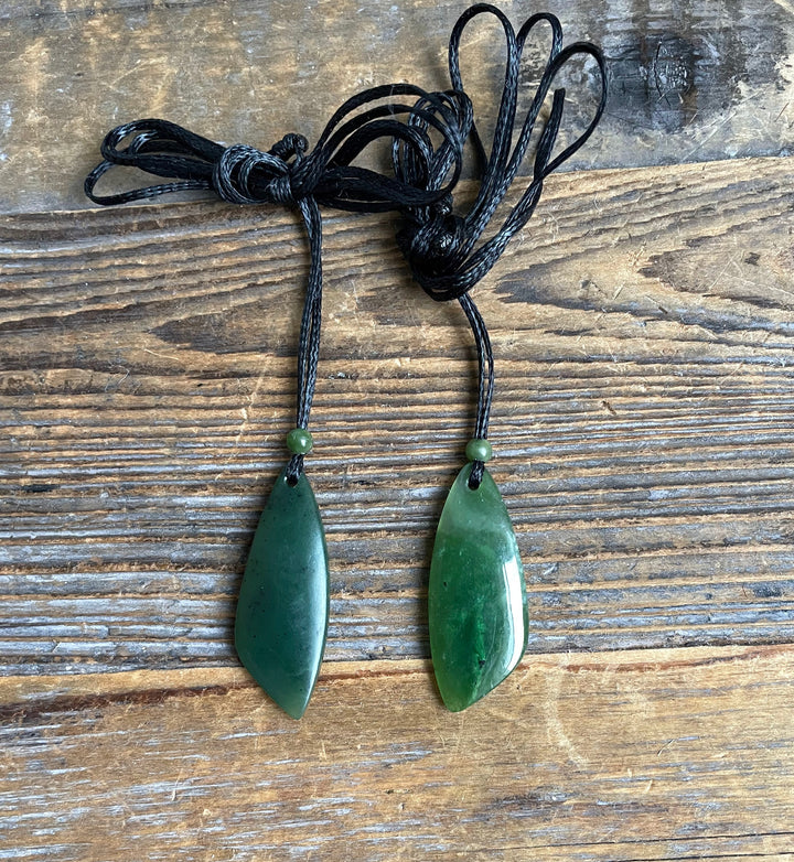 Two green jade teardrop pendants on tangled black cords with small green beads at the top of each