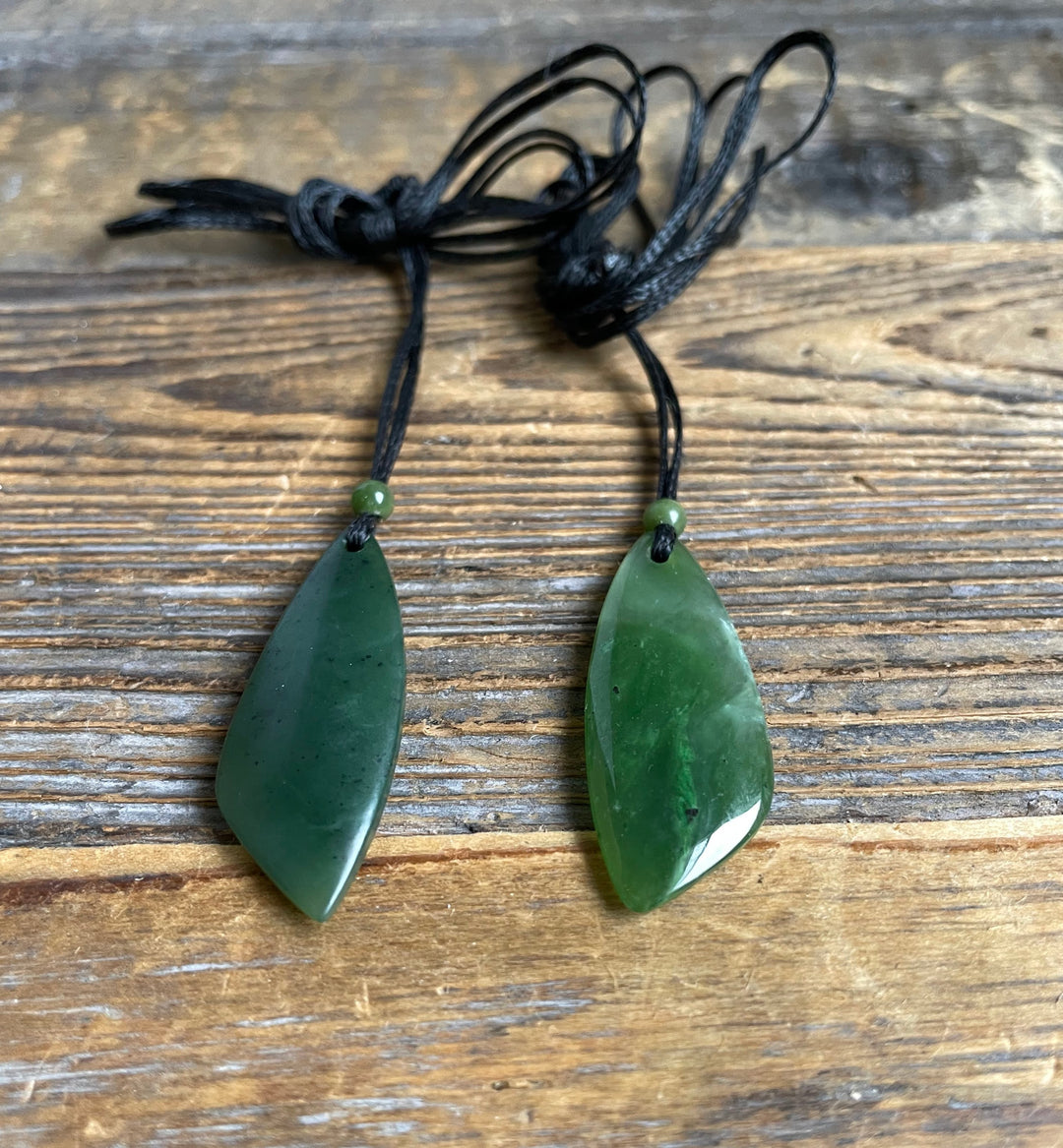 Two green jade teardrop pendants on black cords with small green beads above each pendant