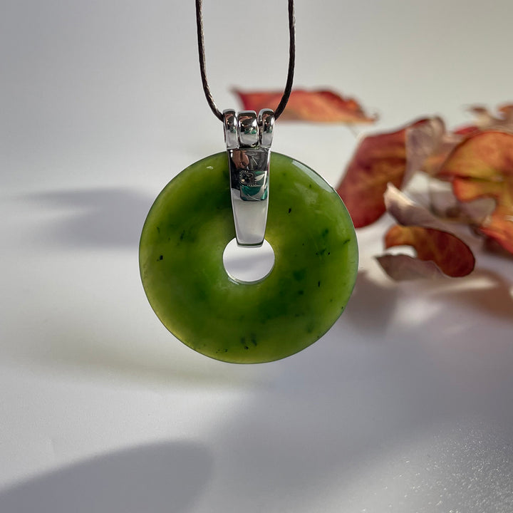 Green jade donut pendant with a silver bail on a black cord