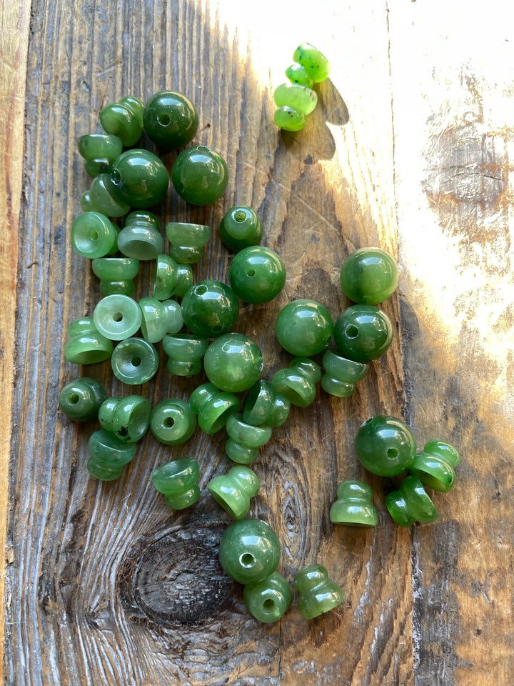 Pile of A Grade 10mm Canadian jade beads including guru bead and 3 hole shapes on weathered wood.