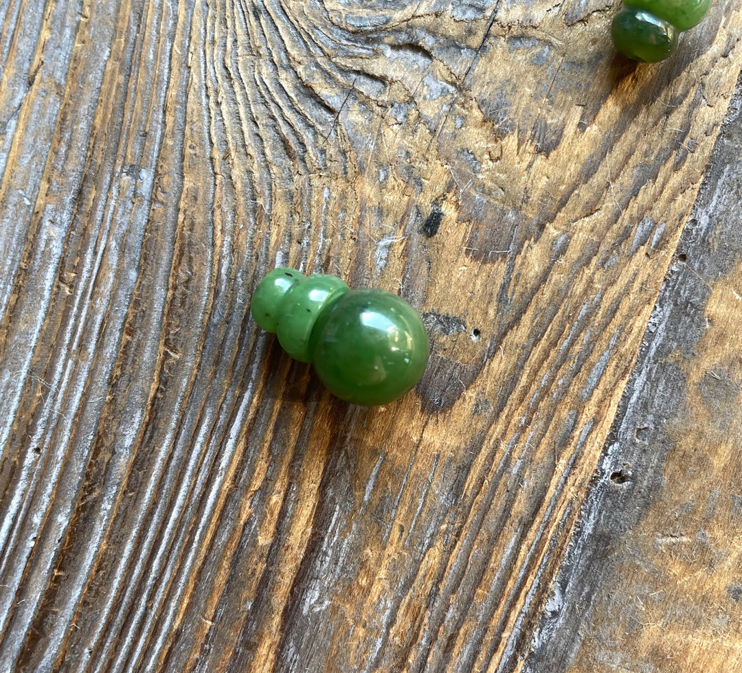 Single glossy green jade bead with a drilled hole on a textured wood background.