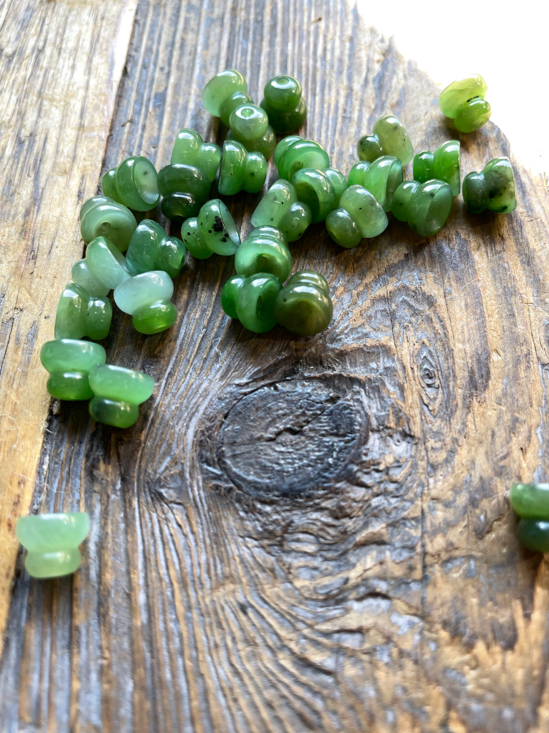Close up of 10mm Canadian jade beads scattered on a rustic wooden surface with drilled holes for stringing.