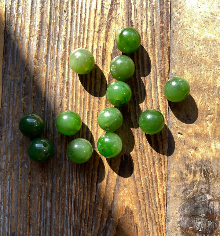 Group of 10mm green jade beads in varying shades spread on a wooden surface