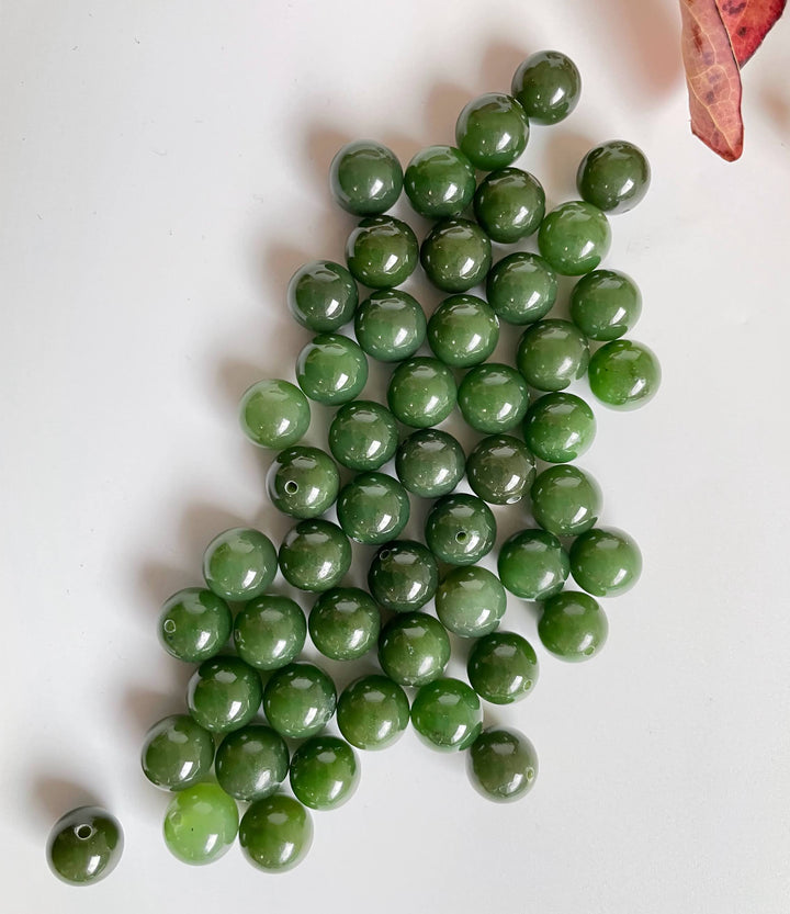 Cluster of glossy green jade beads on a white surface with a dried leaf in the corner