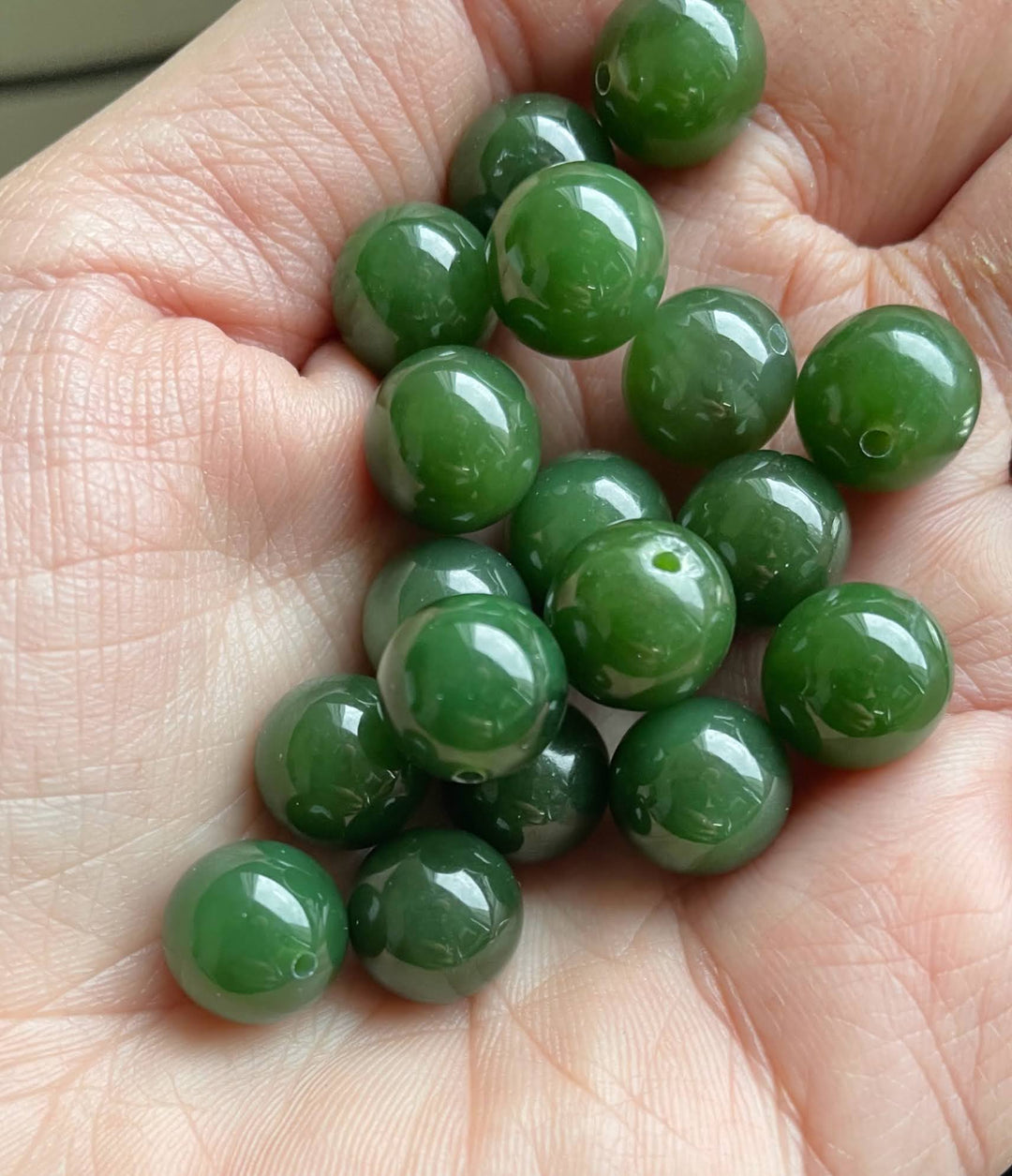 Polished green jade beads held in a palm, showing 10mm half drilled Canadian Jade beads