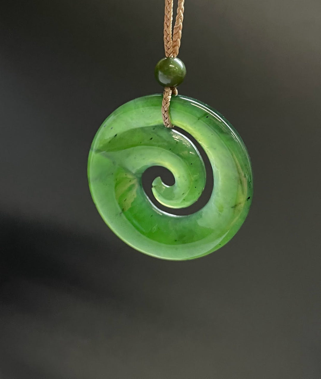 Bright green circular koru pendant with a black spiral motif on a brown cord