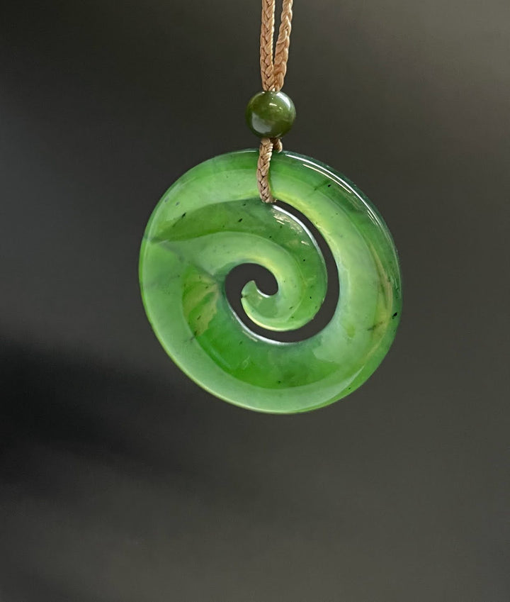 Bright green circular koru pendant with a black spiral motif on a brown cord