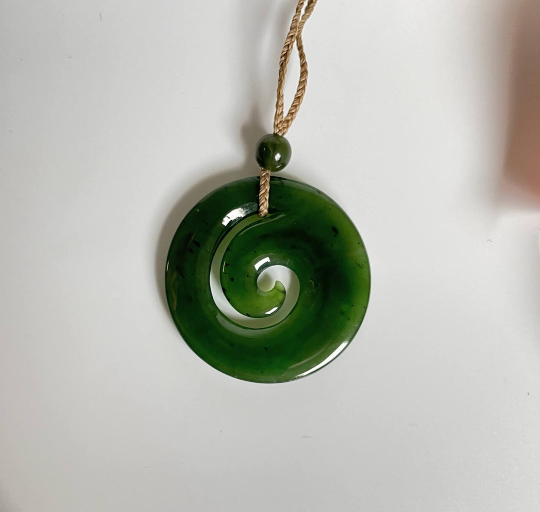 Close up of green spiral koru pendant with hollow center suspended by a braided cord