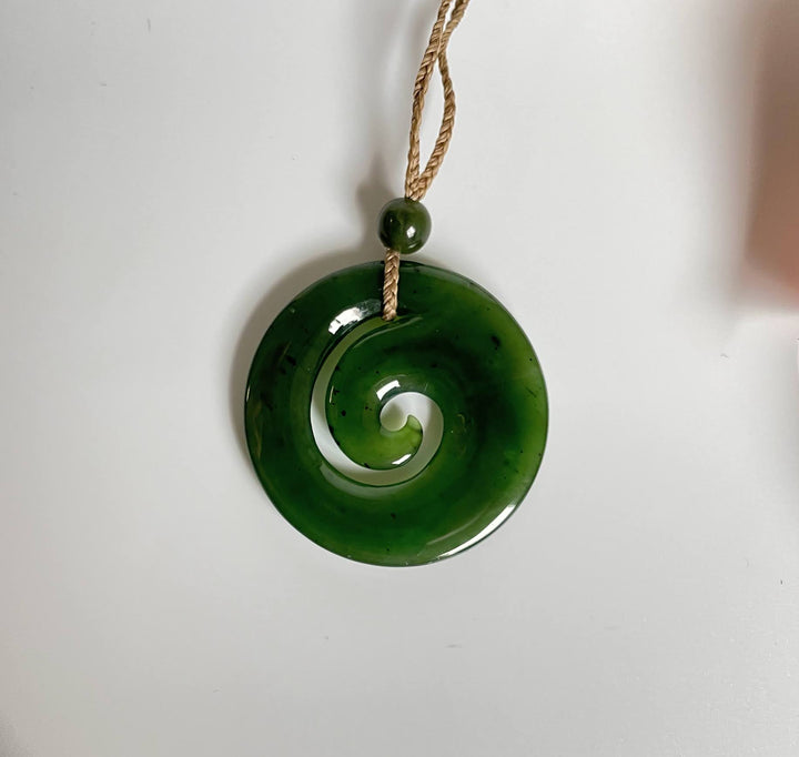 Close up of green spiral koru pendant with hollow center suspended by a braided cord